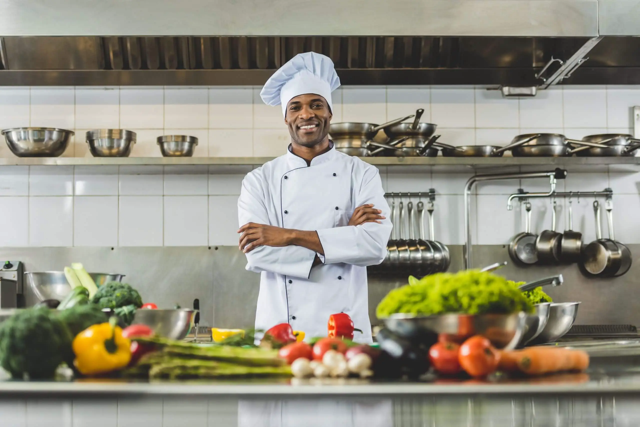 handsome african american chef standing at restaurant kitchen with crossed arms and looking at you