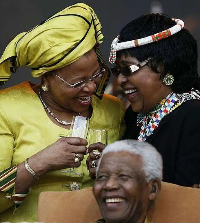 Winnie Mandela smiling with her friend wearing yellow and Champaign glasses. Neilson Mandela in the front