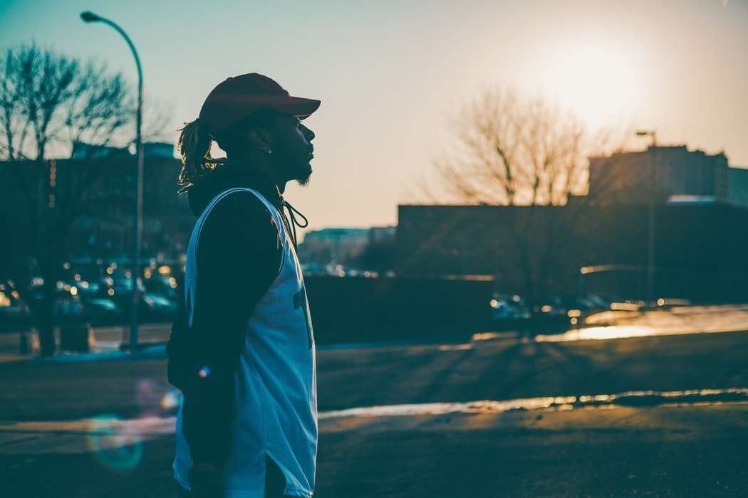 Black man depressed looking at the city with hat on and a jersey