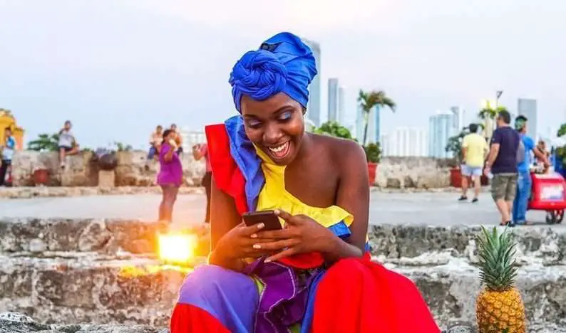 Black Women laughing wearing a blue head wrap on her I phone