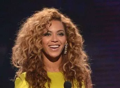 Beyonce smiling in a yellow shirt on stage