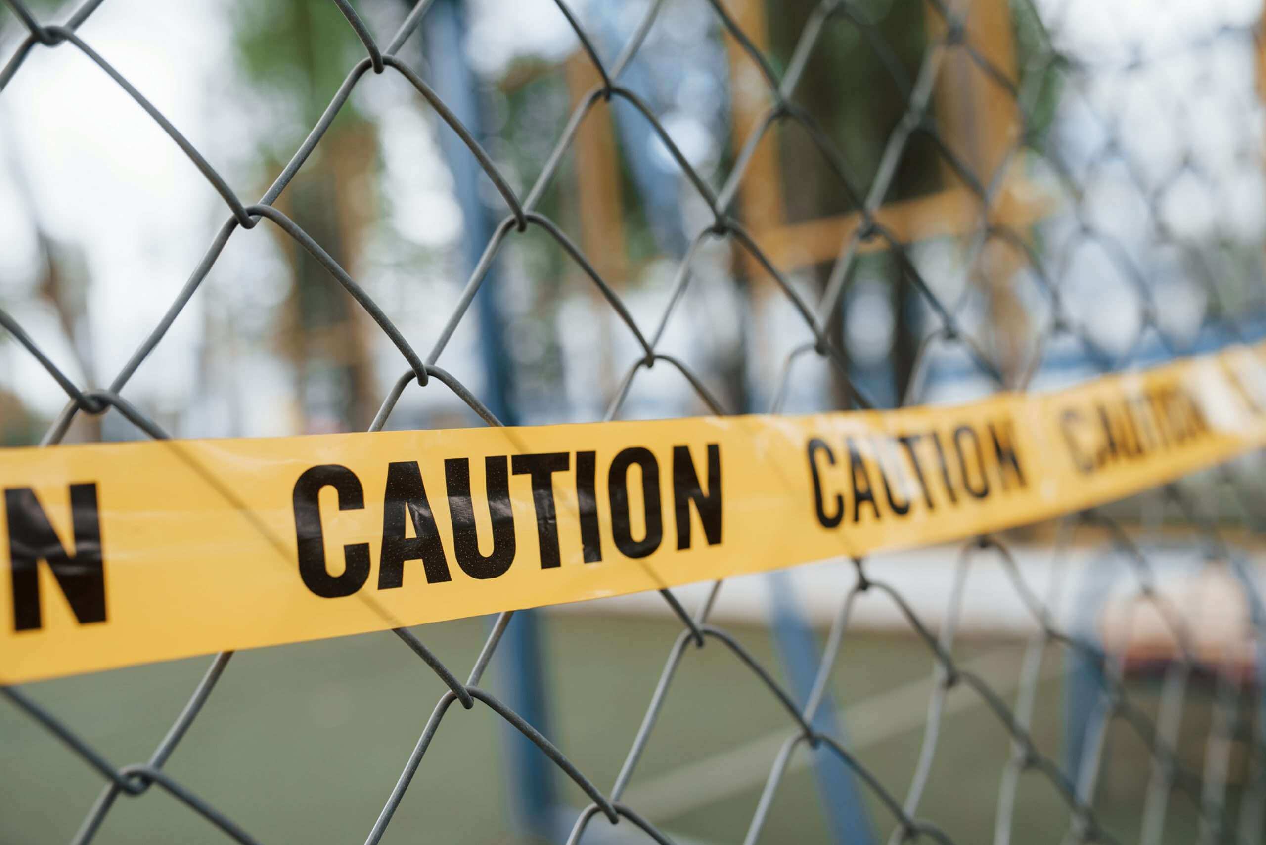 Yellow caution tape on the metal fence at daytime. Crime scene