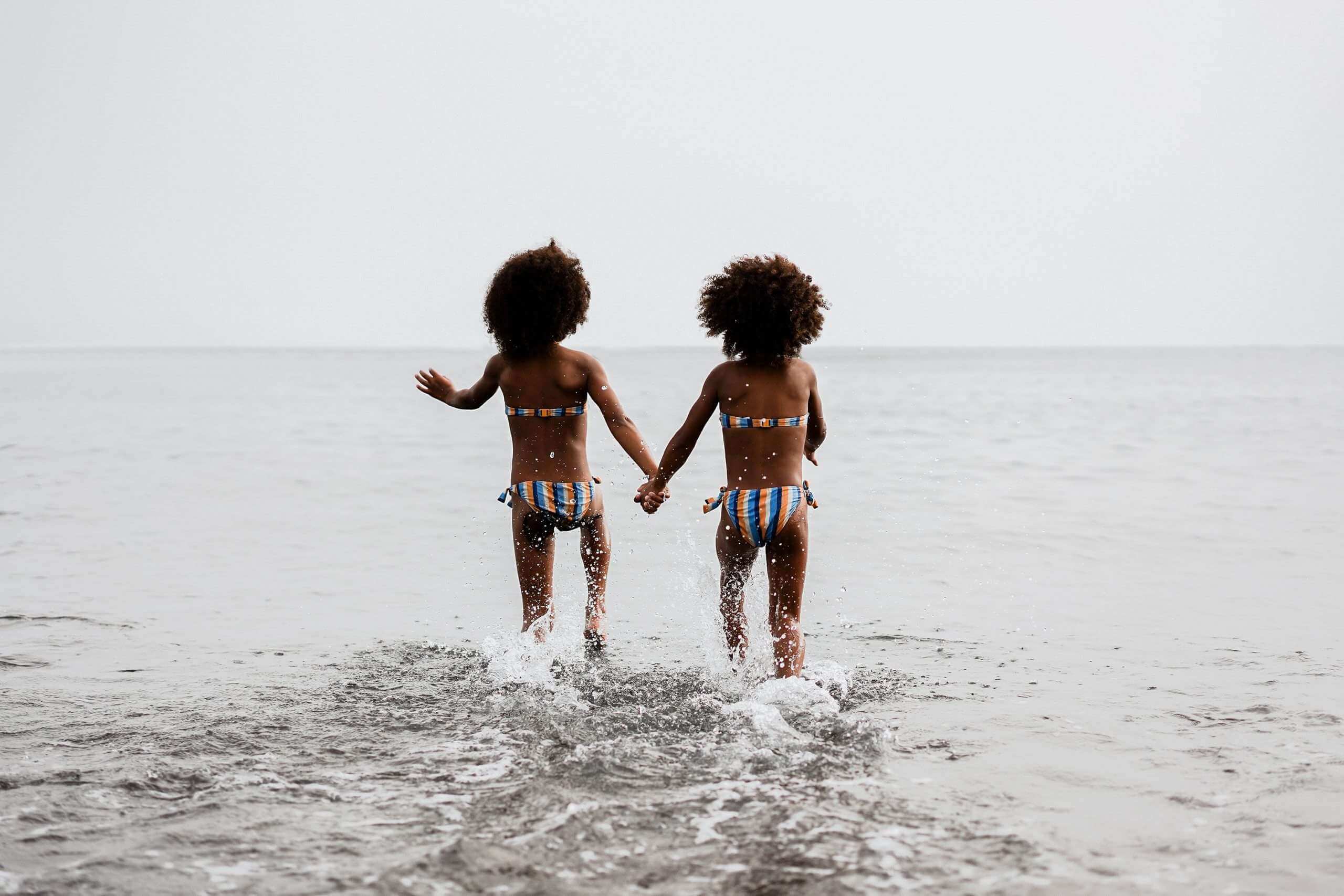 Black twins holding hands running in the beach