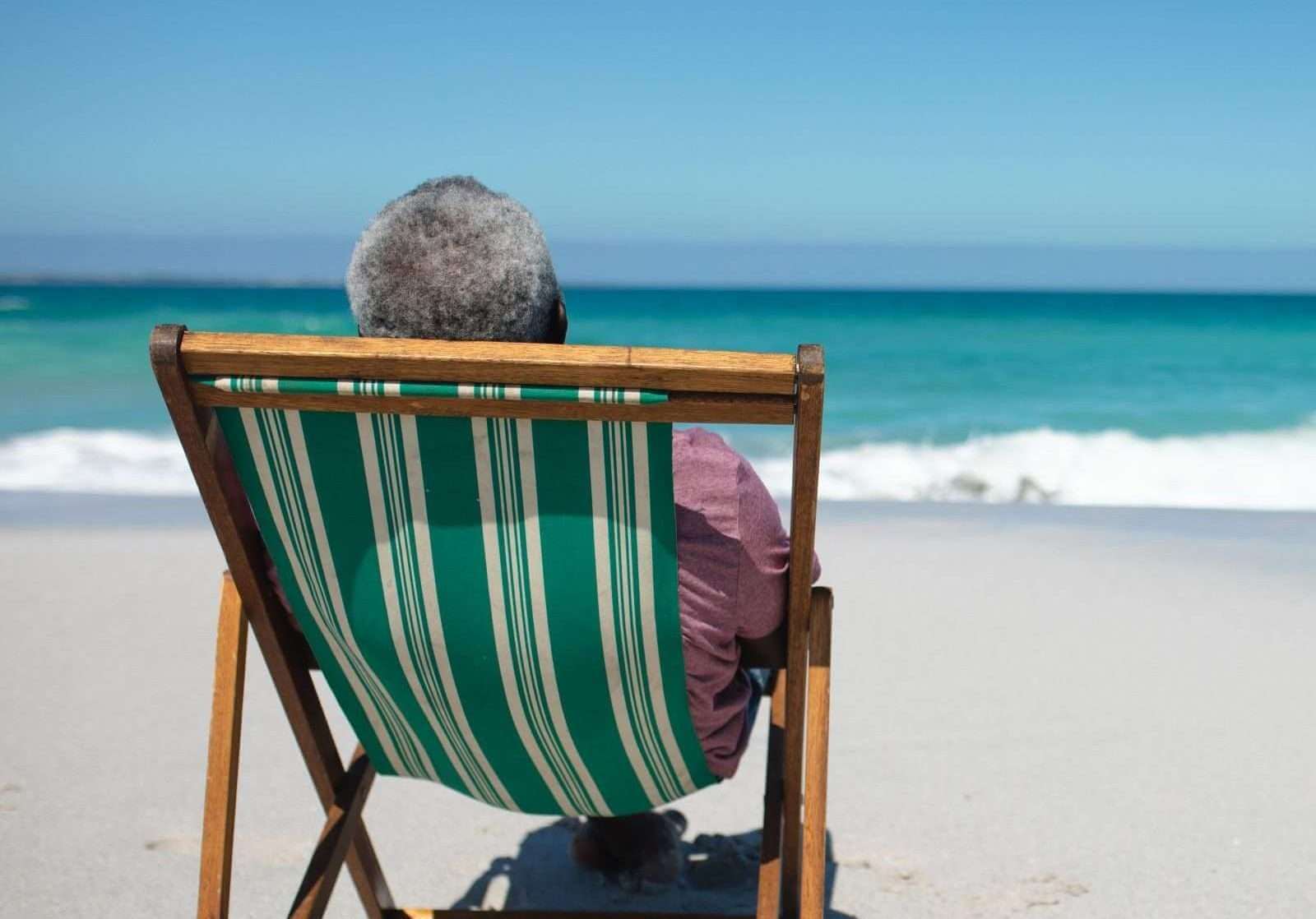 Black older black man sitting on the beach looking at the waves