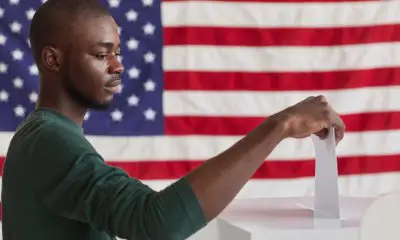 Black Man casting his ballot to vote in front of a red flag