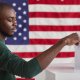 Black Man casting his ballot to vote in front of a red flag