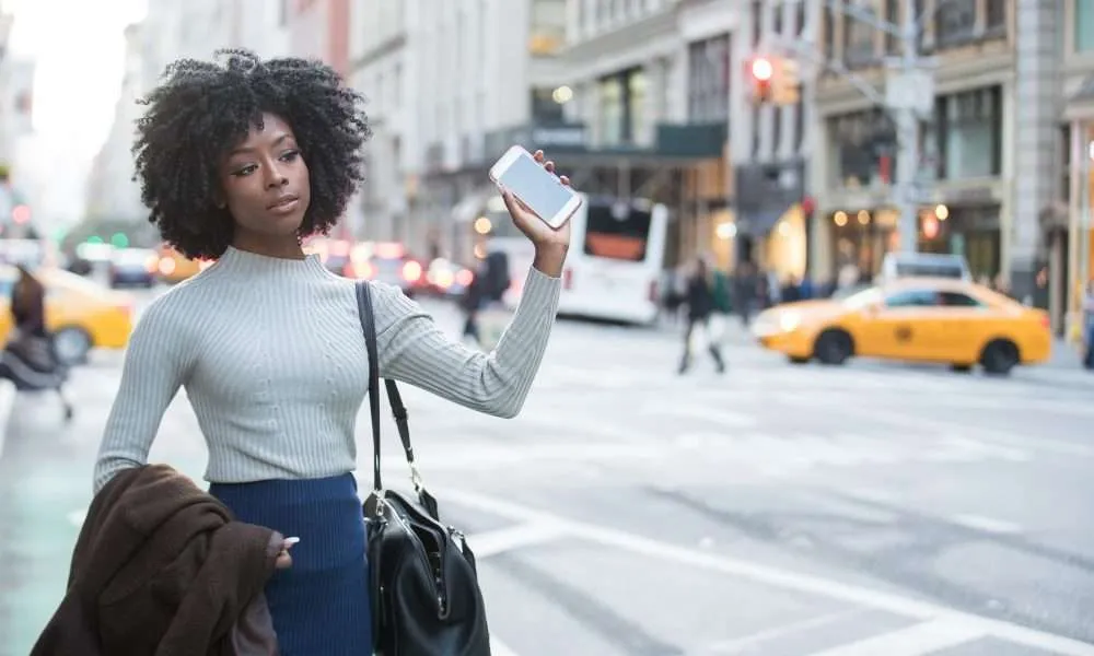 Black business women with natural hair holding up a I phone in the city
