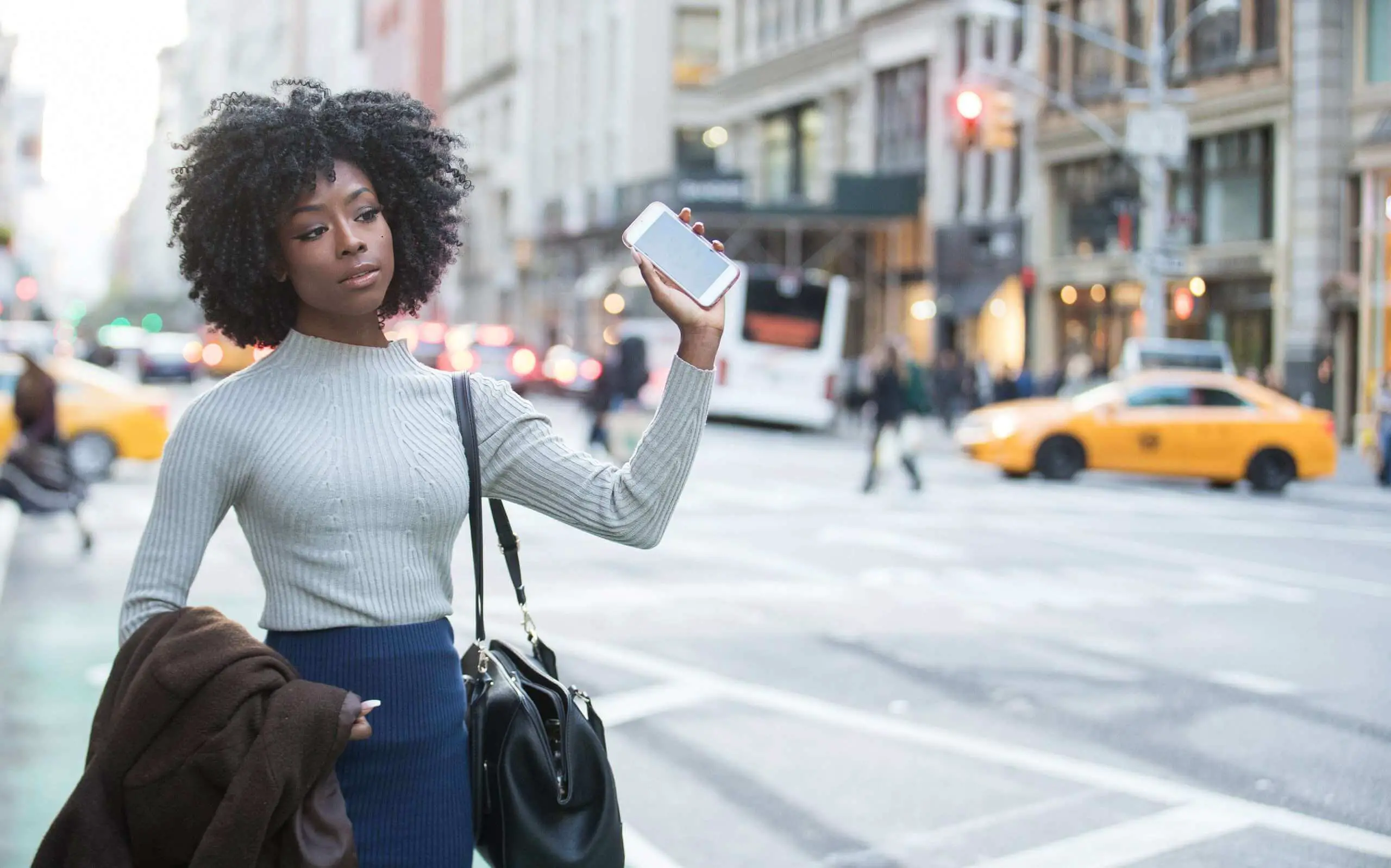 Black business women with natural hair holding up a I phone in the city