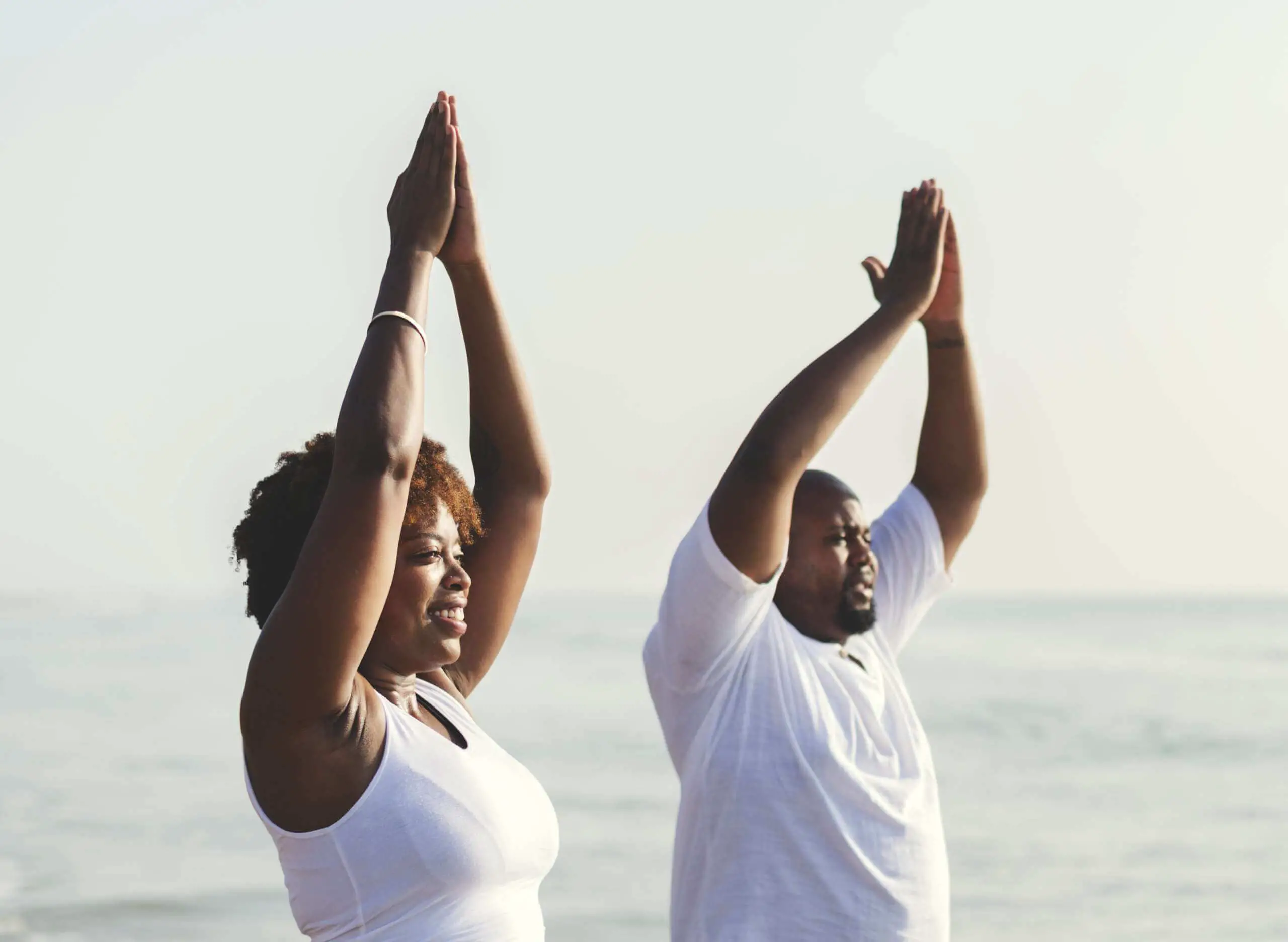 black couple doing yoga at the beach