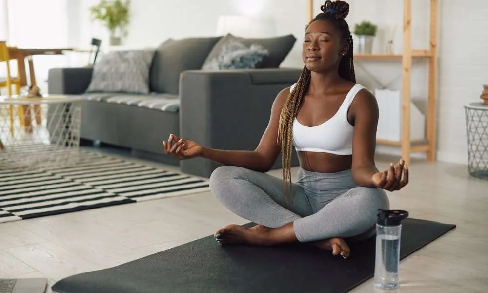 Young African American woman meditating in lotus pose while working out at home.