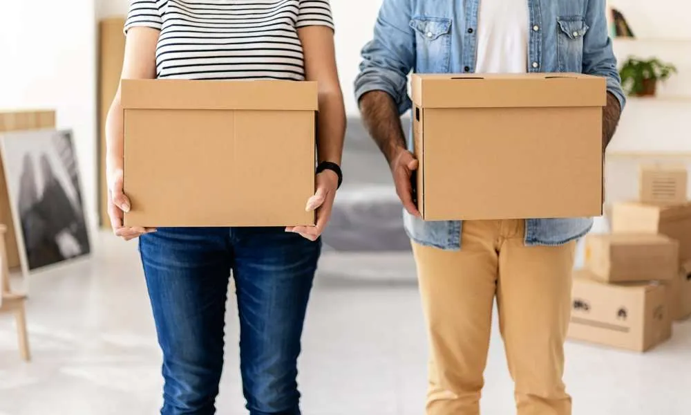 Young couple carrying cardboard boxes at new home before unpacking