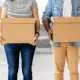 Young couple carrying cardboard boxes at new home before unpacking